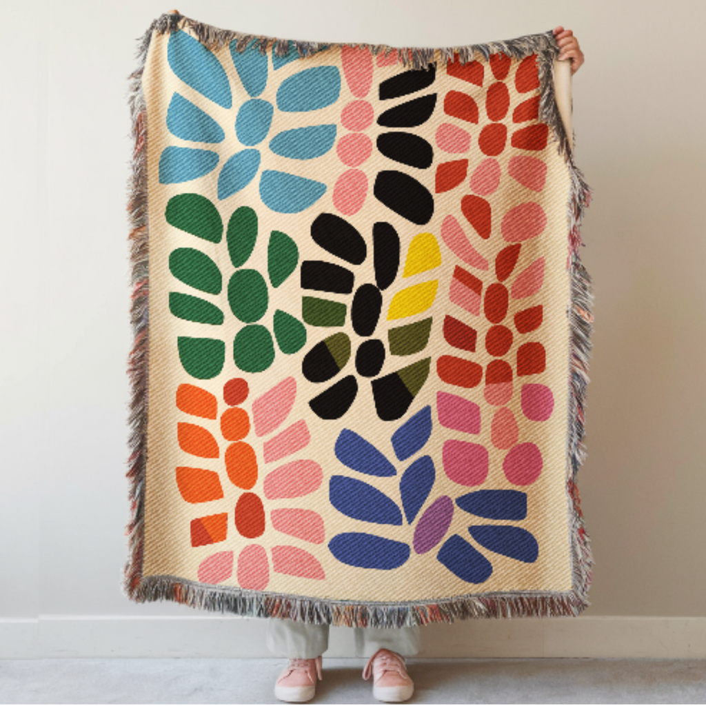 Colorful floral-patterned woven blanket held by a person against a plain background