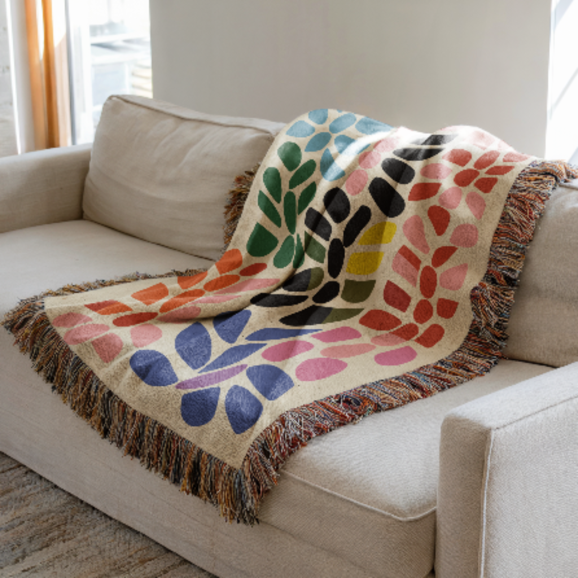 Colorful patterned woven blanket draped over a beige sofa in a bright room.