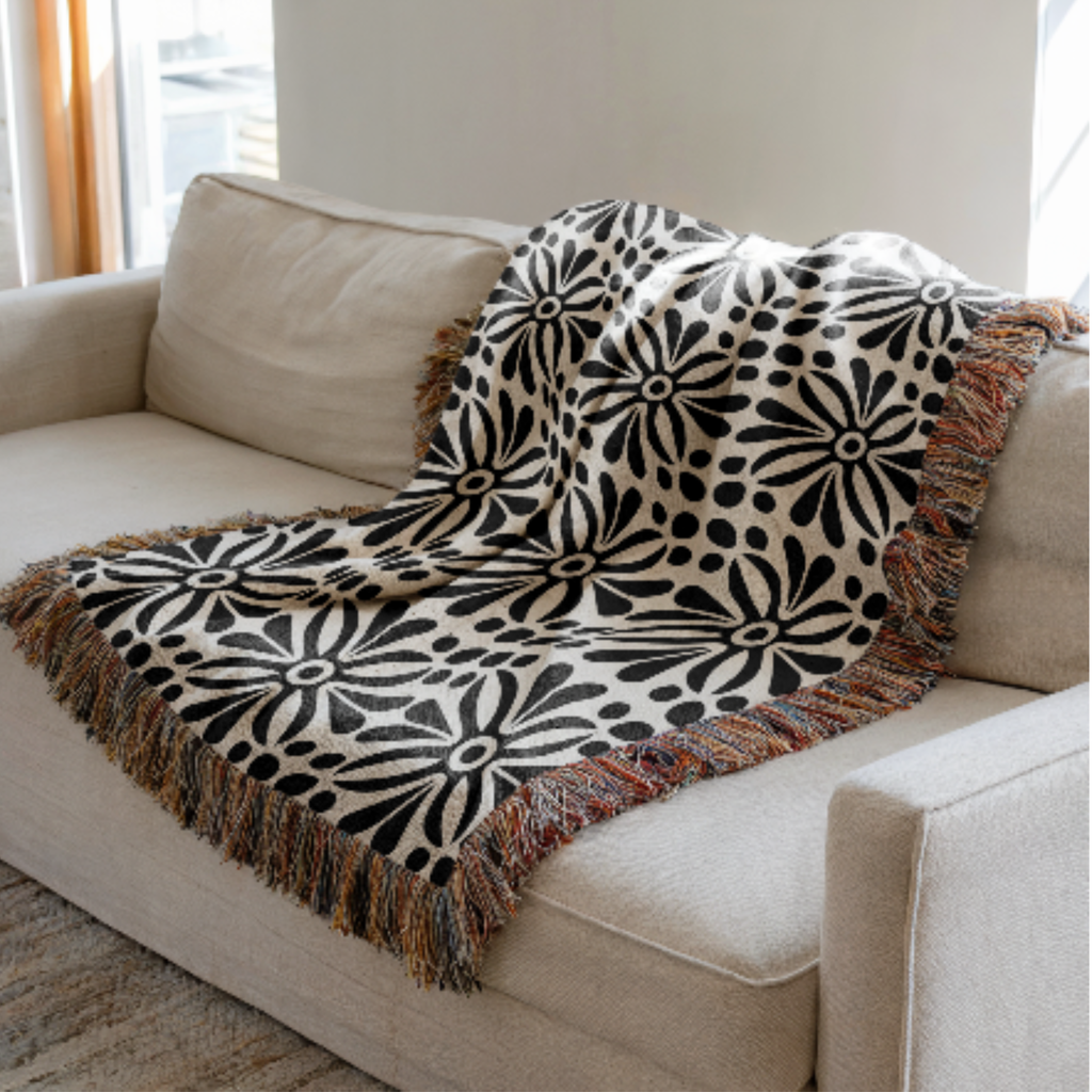 Black Abstract Floral Woven Blanket with fringes on a beige sofa.