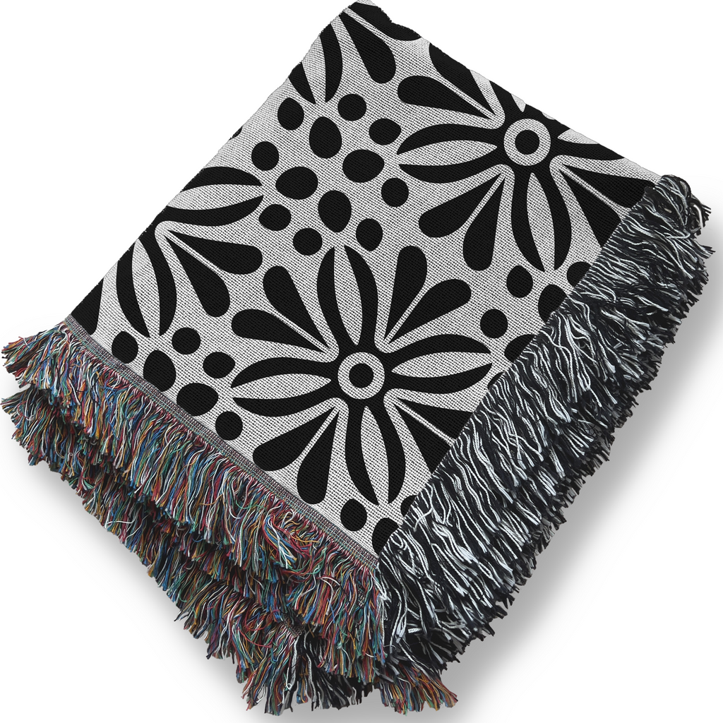 Black and white floral patterned throw blanket with colorful fringe on a white background
