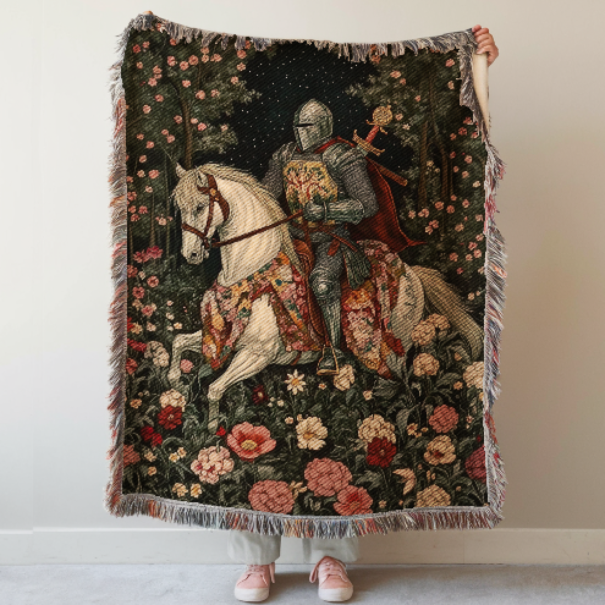 Medieval Knight Woven Blanket Tapestry with a knight on a horse surrounded by flowers held by a person against a white wall.
