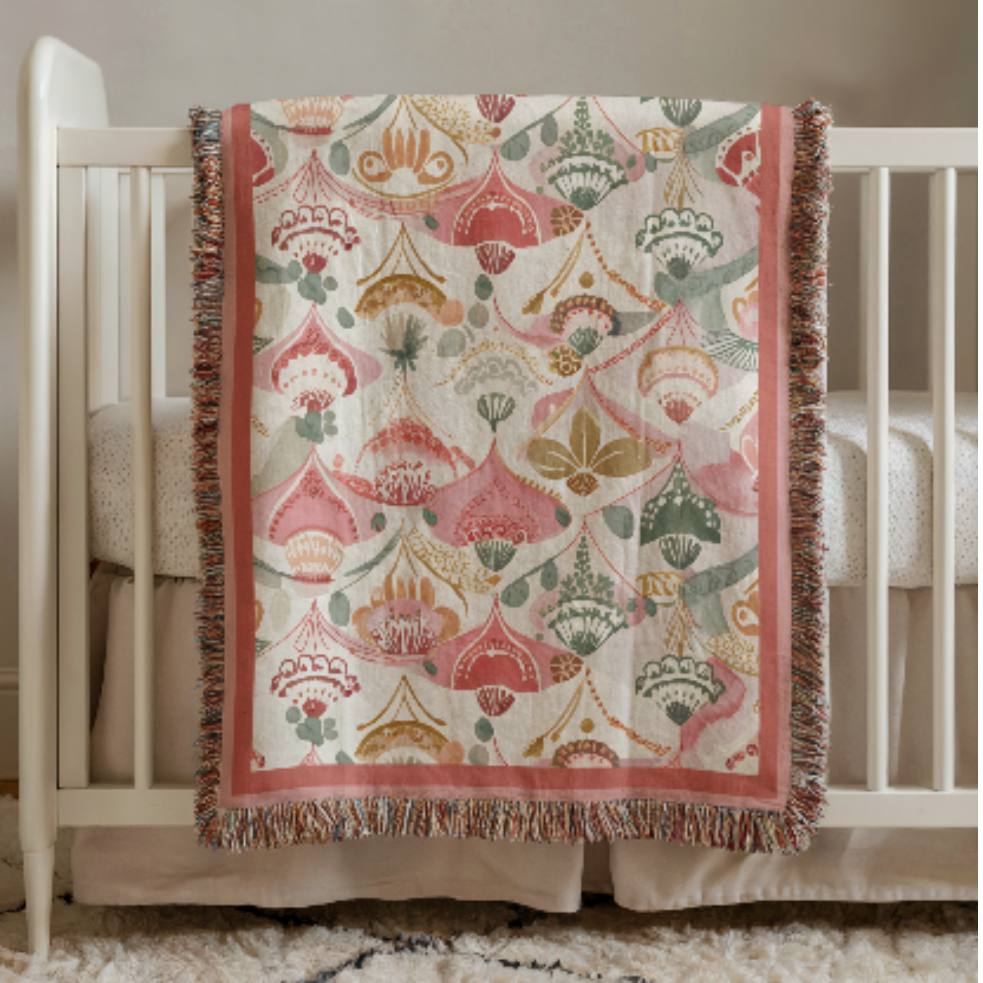 Pink Boho Woven Baby Blanket with a geometric pattern draped over a crib.