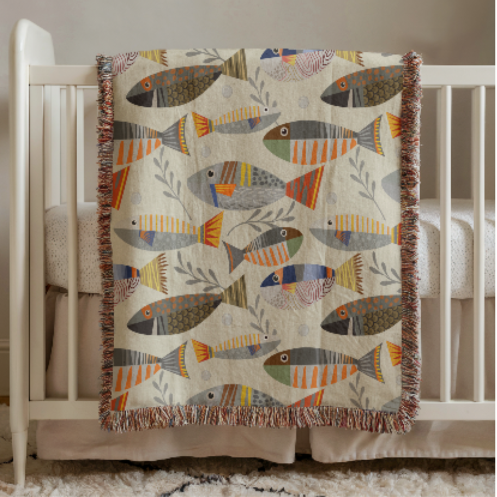 Colorful fish-patterned baby blanket draped over a crib in a nursery setting.