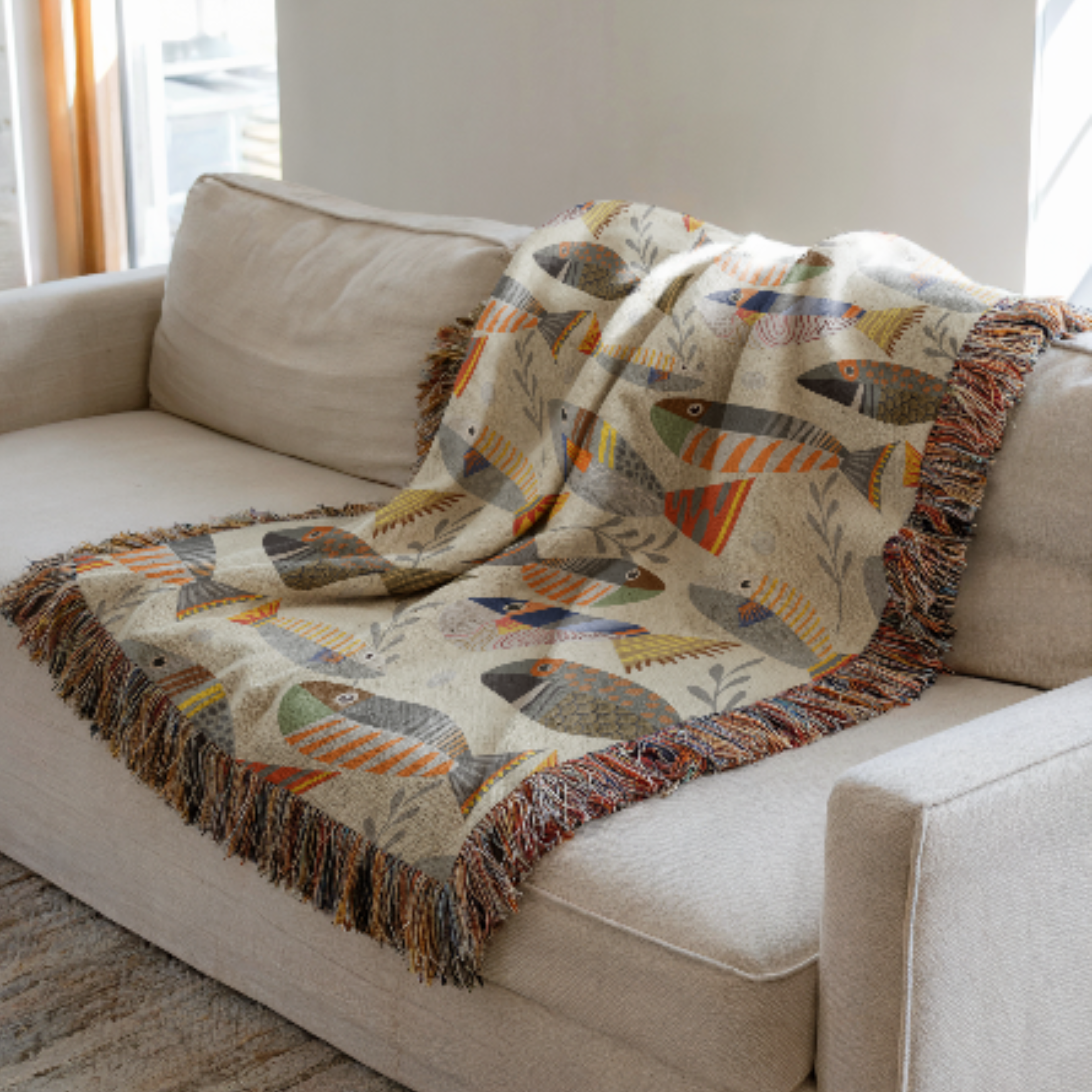 Fish-patterned woven blanket draped over a beige sofa in a living room.